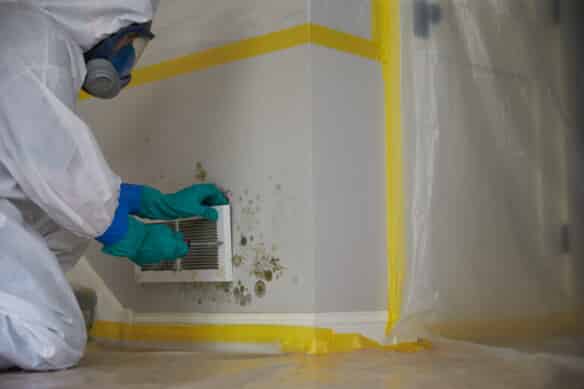 A ServiceMaster technician dressed in protective clothing inspects mold surrounding a vent in a home in Cedar City