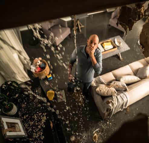 A shocked homeowner looks up at his severely leaking ceiling after weather damage in Hutto, Texas