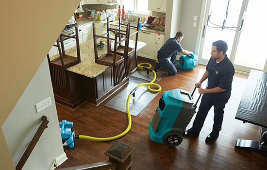 Two ServiceMaster technicians use drying equipment on a home’s kitchen floor during flood damage restoration in Cedar City, Utah