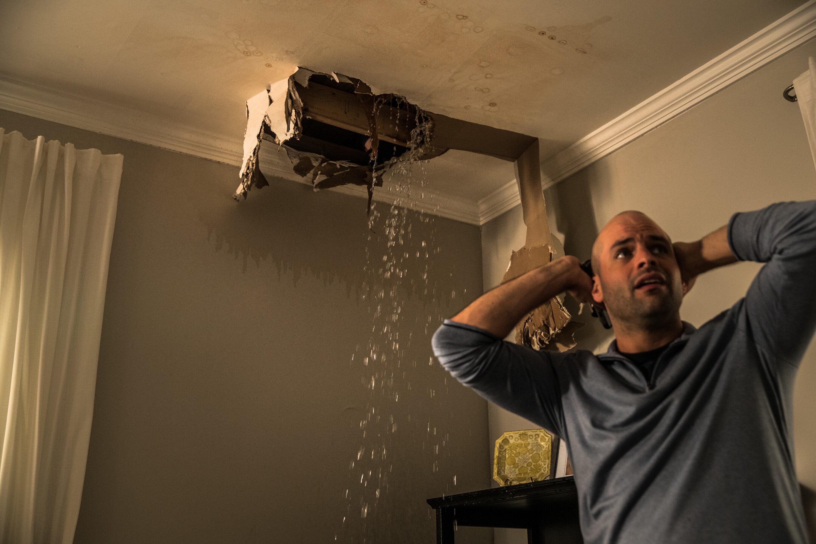 A distressed homeowner standing near his ceiling with a leaking hole caused by storm damage in Spokane, Washington