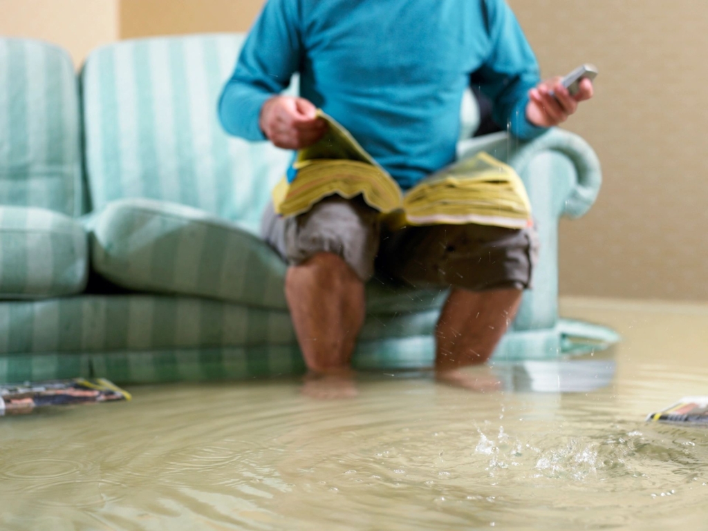 man in a flooded room, sitting on couch with feet under water 
