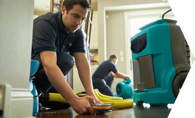 A ServiceMaster Restore flood restoration tech using a moisture meter on a wet kitchen floor