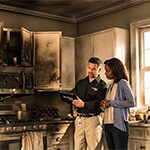 Two individuals discussing by a fire damaged kitchen.