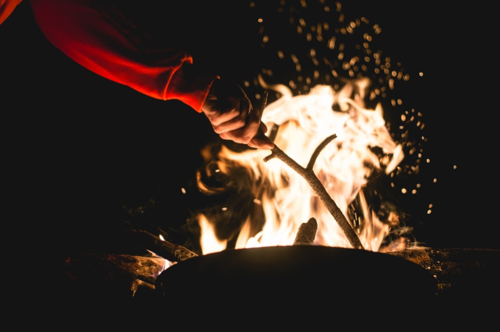 Hand stoking a fire with a branch