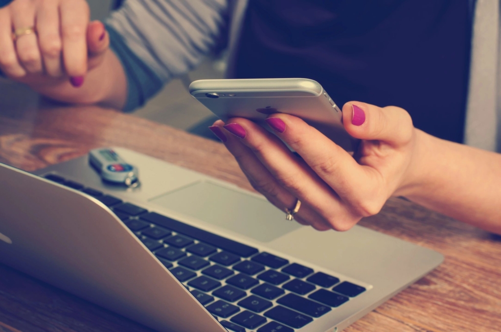 hands holding a phone and in front of a lap top