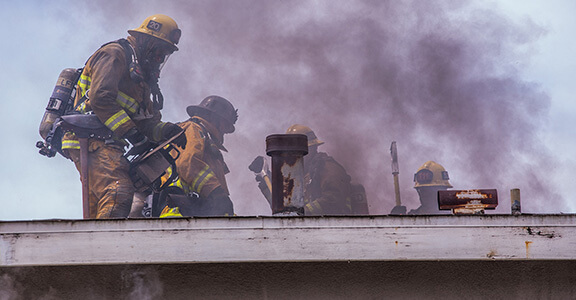 Firefighters standing on roof of smoking building