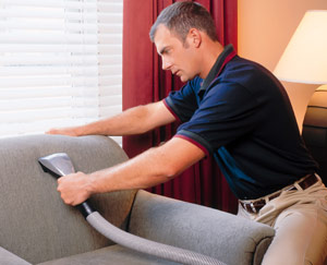 Man cleaning a couch with a vacuum