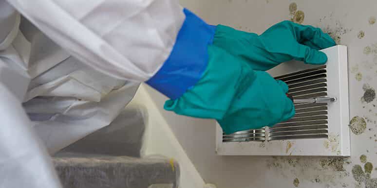 A person with  gloves cleaning off a moldy vent