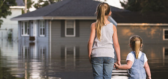 Two Children Holding Hands in Front of Flooded House