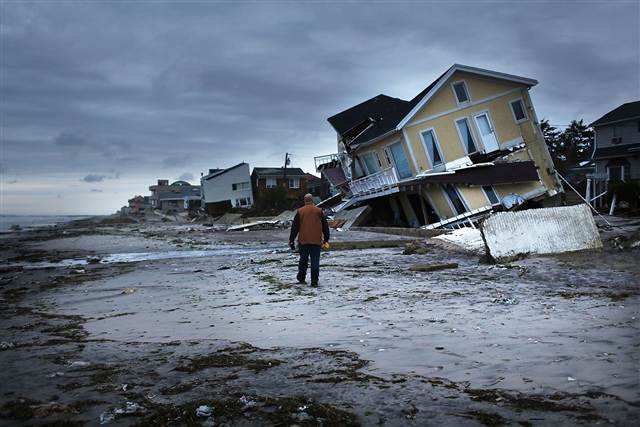 Man walking on the beach next to destroyed homes